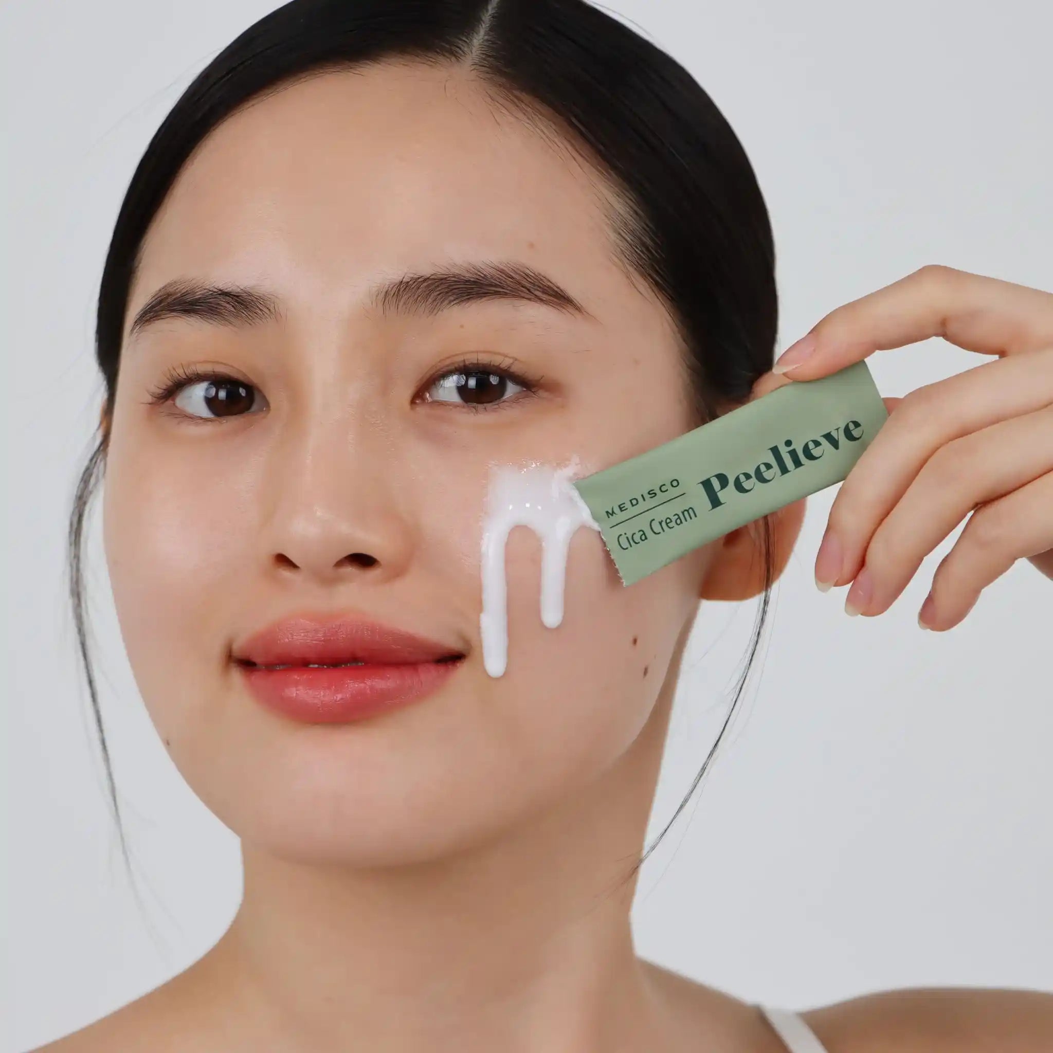 Woman applying cream to her face with a green tube labeled 'Medesco Peelieve' against a white background