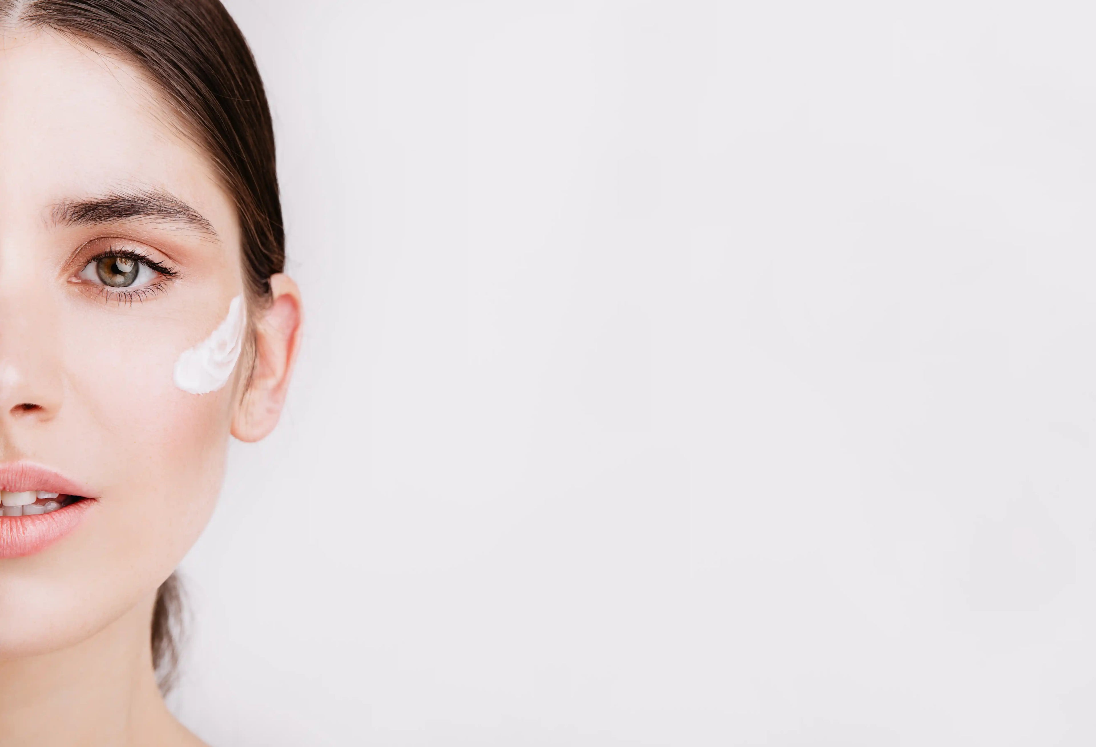 Woman applying cream to her face with a plain background